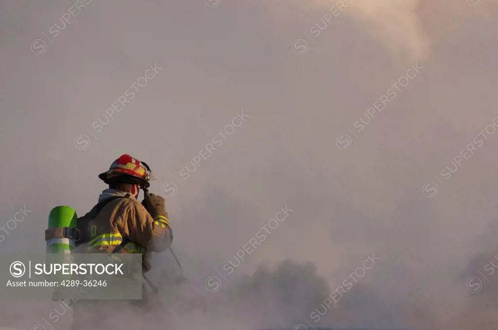 An Anchorage Fire Department firefighter stands atop the roof of a downtown motel while working to extinguish the blaze, Southcentral Alaska, Winter