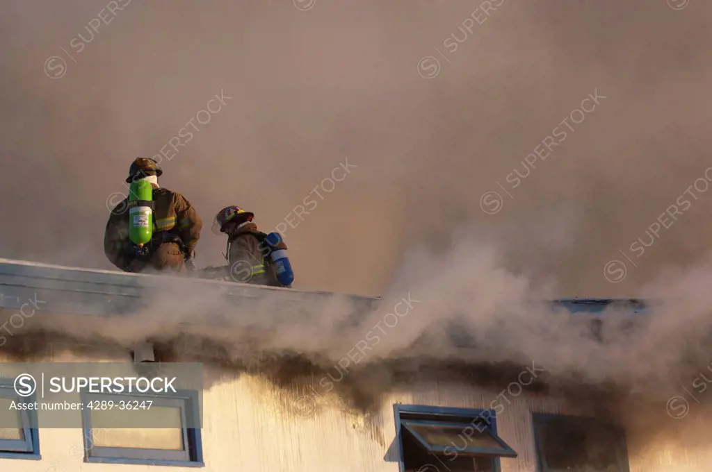 Two Anchorage Fire Department firefighters stand atop the roof of a downtown motel while working to extinguish the blaze, Southcentral Alaska, Winter