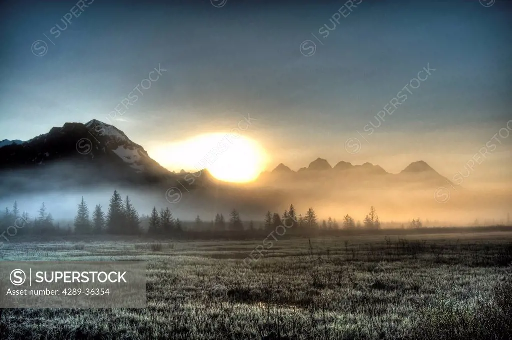 Morning fog hangs on the ground near the Copper River Highway as the sun rise over the Chugach Mountains, Chugach National Forest, Southcentral Alaska...