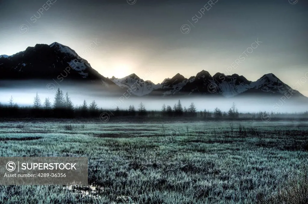 Morning fog hangs on the ground near the Copper River Highway as the sun rise over the Chugach Mountains, Chugach National Forest, Southcentral Alaska...