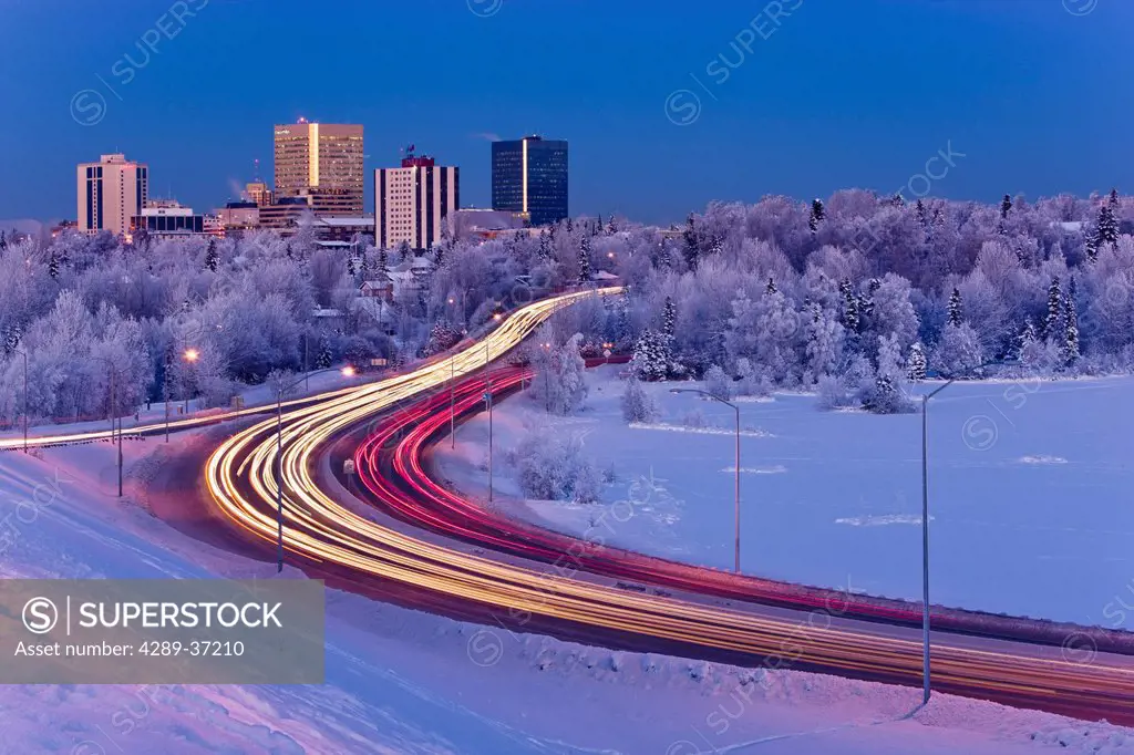 Alpenglow Over The Anchorage Skyline With The Lights From Traffic On Minnesota Blvd. In The Foreground During Winter, Southcentral Alaska