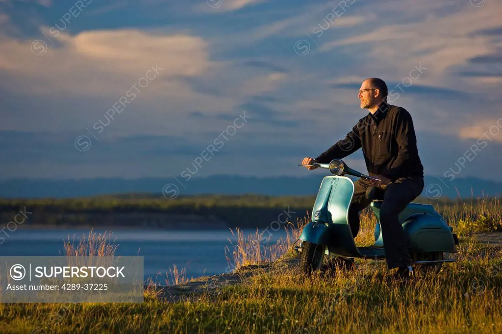 Man Sitting On A Vintage 1959 Vespa Motor Scooter Overlooking Knik Arm, Tony Knowles Coastal Trail, Anchorage, Alaska