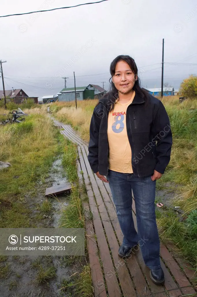 Portrait Of 20-Something Yupik Native Woman On Boardwalk W/Akiachak Background We Alaska Autumn