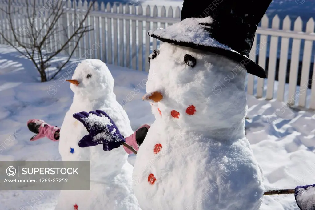 Pair Of Snowmen Standing Next To A White Picket Fence In The Front Yard Of A Anchorage Home In Winter