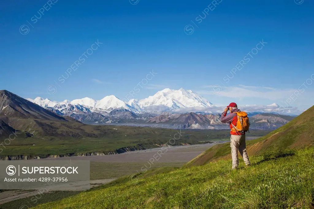 A Senior Male Hiker Stands On The Tundra On A Mountain Side With Mt. Mckinley And The Thorofare River In The Background In Denali National Park; Alask...