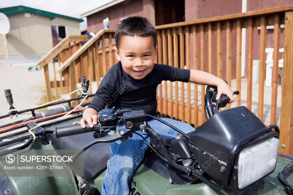 A Young Boy Smiles Playfully While Sitting Atop A Four Wheeler And Holding The Handlebars; Igiugig Bristol Bay Alaska United States Of America