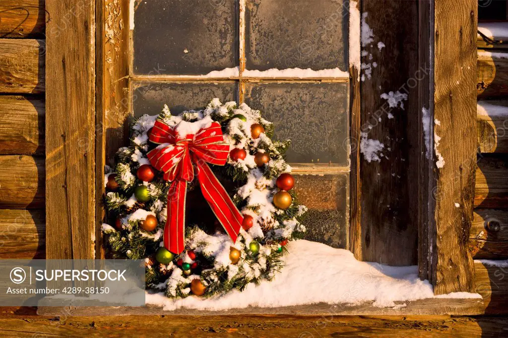 Decorated christmas wreath sits in the windowsill of a rustic log barn mat-su valley in winter;Palmer alaska usa