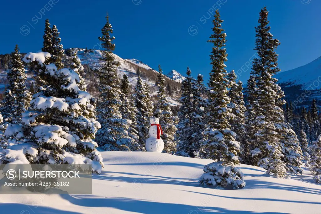 Snowman wearing a red scarf and black top hat standing in front of a snowcovered spruce forest chugach mountains;Anchorage alaska usa