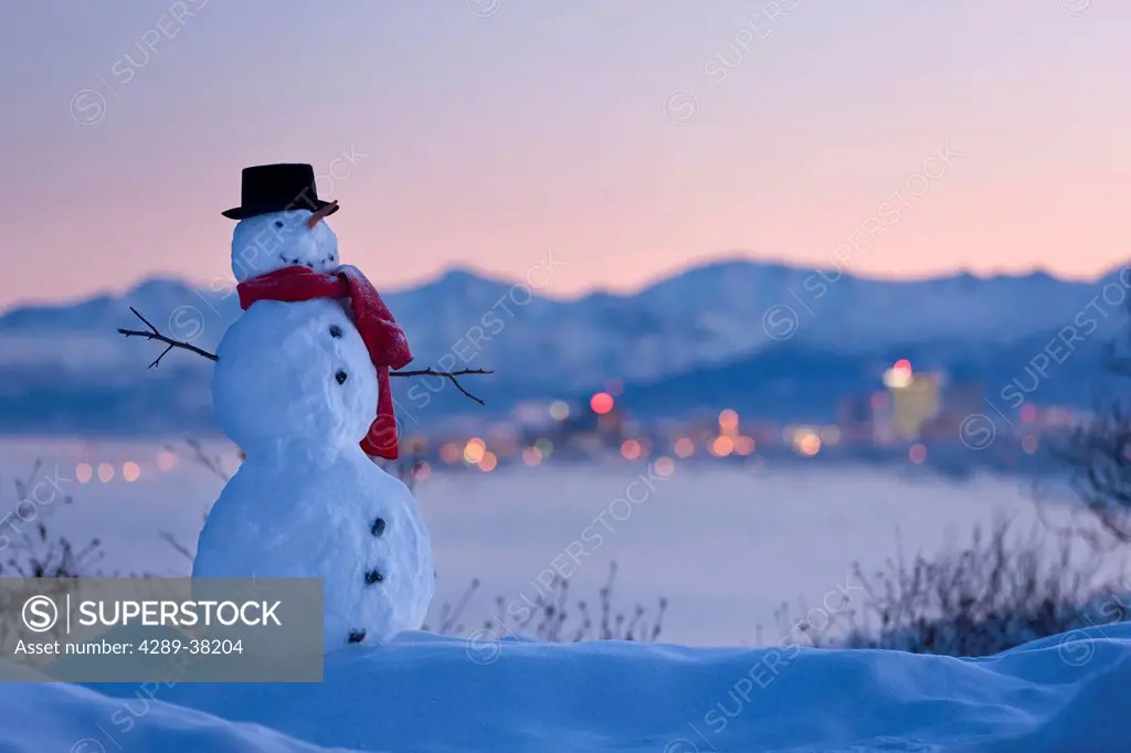 Snowman in front of downtown skyline at dawn knik arm and chugach mountains in the background;Anchorage alaska usa