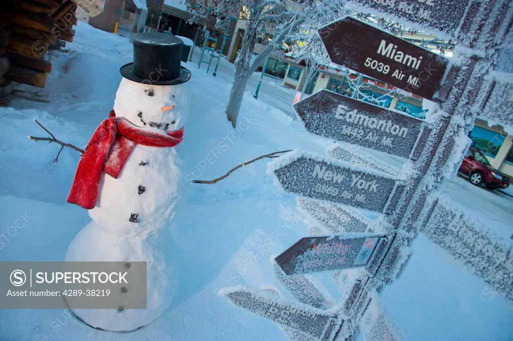 Snowman wearing a black top hat and red scarf standing next to the mileage signpost downtown;Anchorage alaska usa