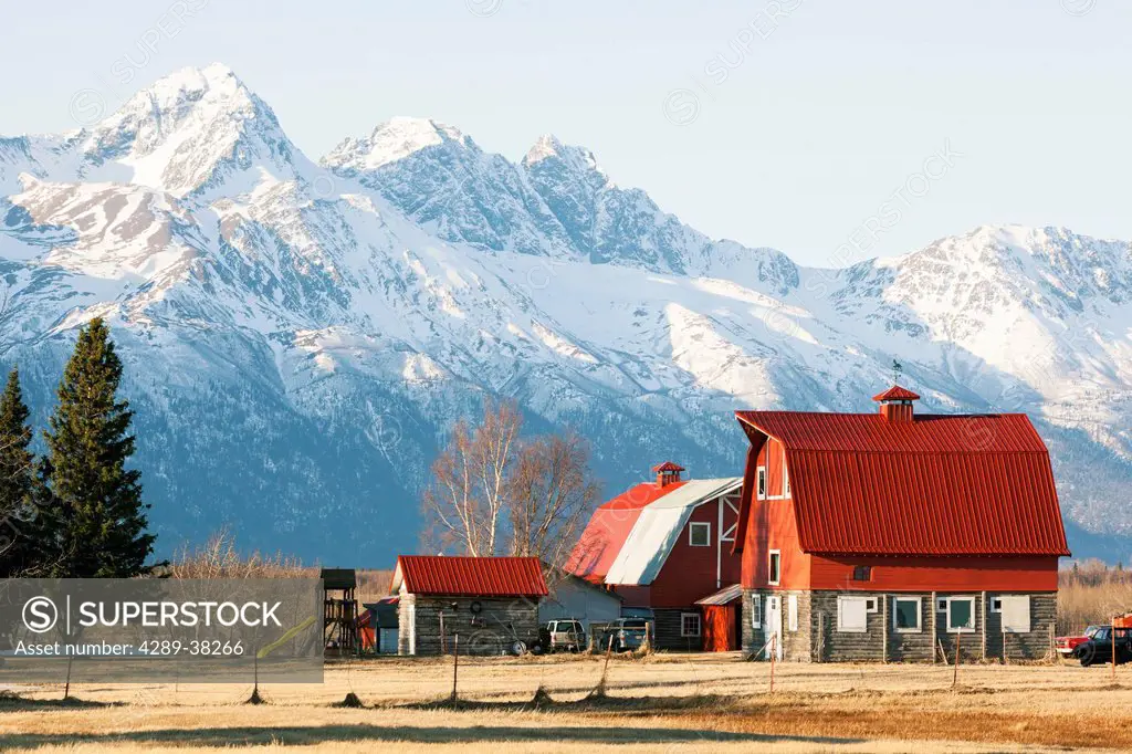 Scenic view of a farm homestead with red barns and Chugach mountains in the background, Palmer, Mat-Su Valley, Southcentral Alaska, Spring
