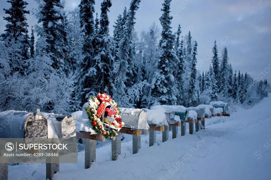 Several mailboxes lined up in a row with one decorated with a Christmas wreath during winter in Alaska