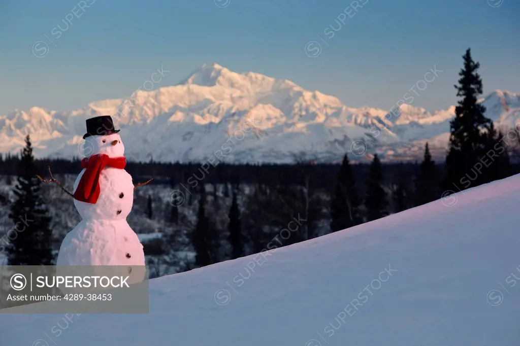 Snowman red scarf and black top hat sitting on a hillside with Mount McKinley in the background at sunrise, Denali State Park, Southcentral Alaska, Wi...
