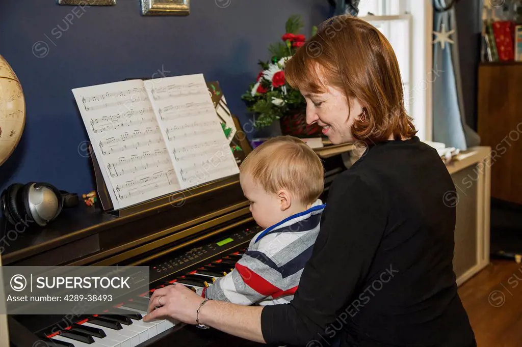 A 15 month old Caucasion boy sits on his mother's lap while she helps him play an electronic piano in their home in Willimantic, Connecticut.