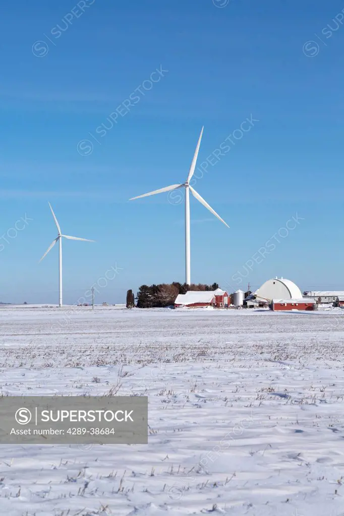 Wind turbines from the Elk Wind Energy Farm rising above a farm and the snow covered landscape near Greeley in Northeast Iowa, Winter