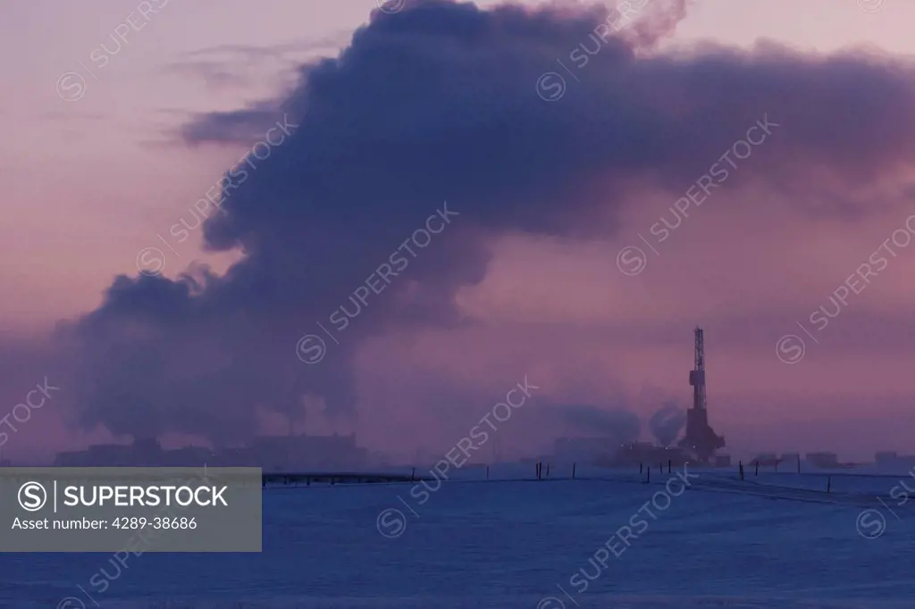 Exhaust fumes from Flow Station 3 fill the sky and a Doyon Drilling Rig at dusk in the Prudhoe Bay Oil Field, North Slope, Arctic Alaska, Winter