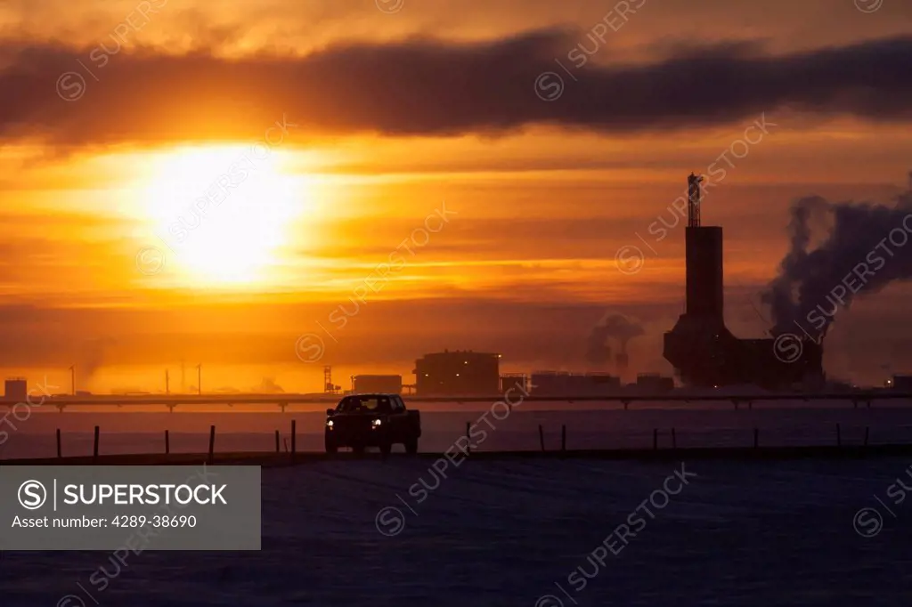 Pickup truck driving down the road with Parker Drilling Rig 273 in the background at Sunrise, Prudhoe Bay Oilfield, North Slope, Arctic, Alaska, Winte...