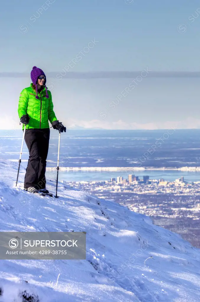 Woman snowshoer taking in the view from Blueberry Hill at the Glen Alps area of Chugach State Park overlooking Anchorage, Southcentral Alaska, Winter,...