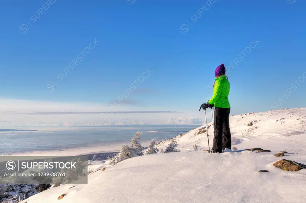Woman snowshoer taking in the view of Cook Inlet and the Alaska Range from Blueberry Hill at the Glen Alps area of Chugach State Park, Anchorage, Sout...