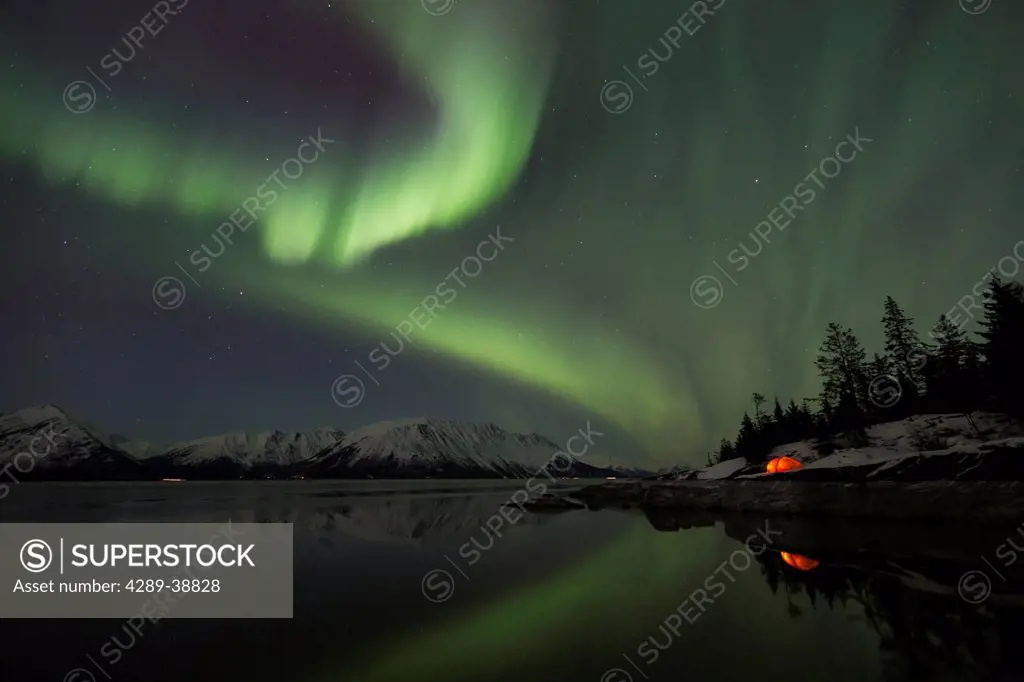 View of the Aurora Borealis (Northern Lights) dancing above the Chugach Mountains with a backpacking tent reflecting in the waters of Turnagain Arm, K...