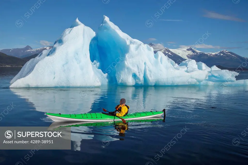 A sea kayaker paddles beside an iceberg in Southeast Alaska's Stephens Passage on a summer evening, Holkham Bay, Tracy Arm. MR_ Ed Emswiler, ID#121720...