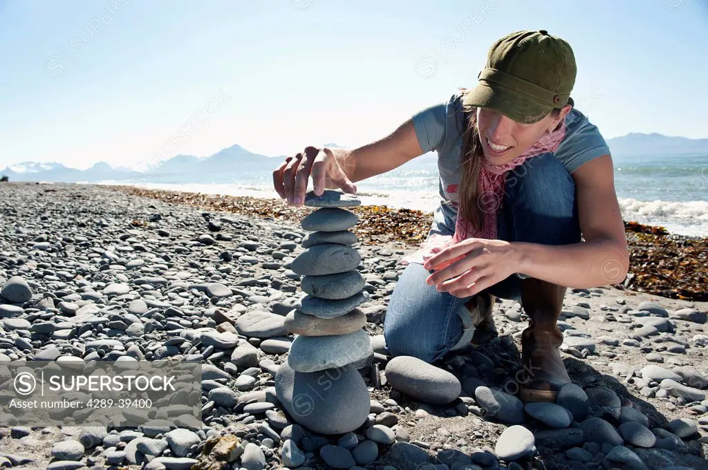 A woman stacks rocks into a cairn on the beach in Homer, Kachemak Bay, Kenai Peninsula, Southcentral Alaska, Summer