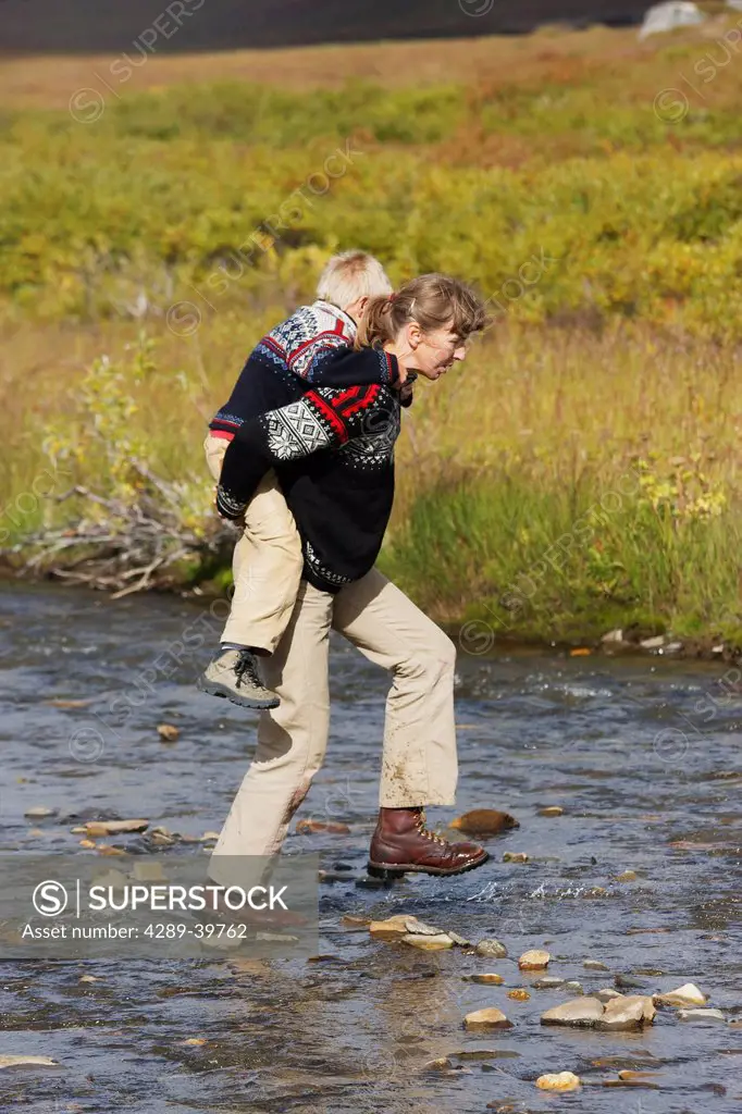 Mom carries boy across Hot Springs Creek to begin a hike near Serpentine Hot Springs, Bering Land Bridge National Preserve (National Park), Northwest ...