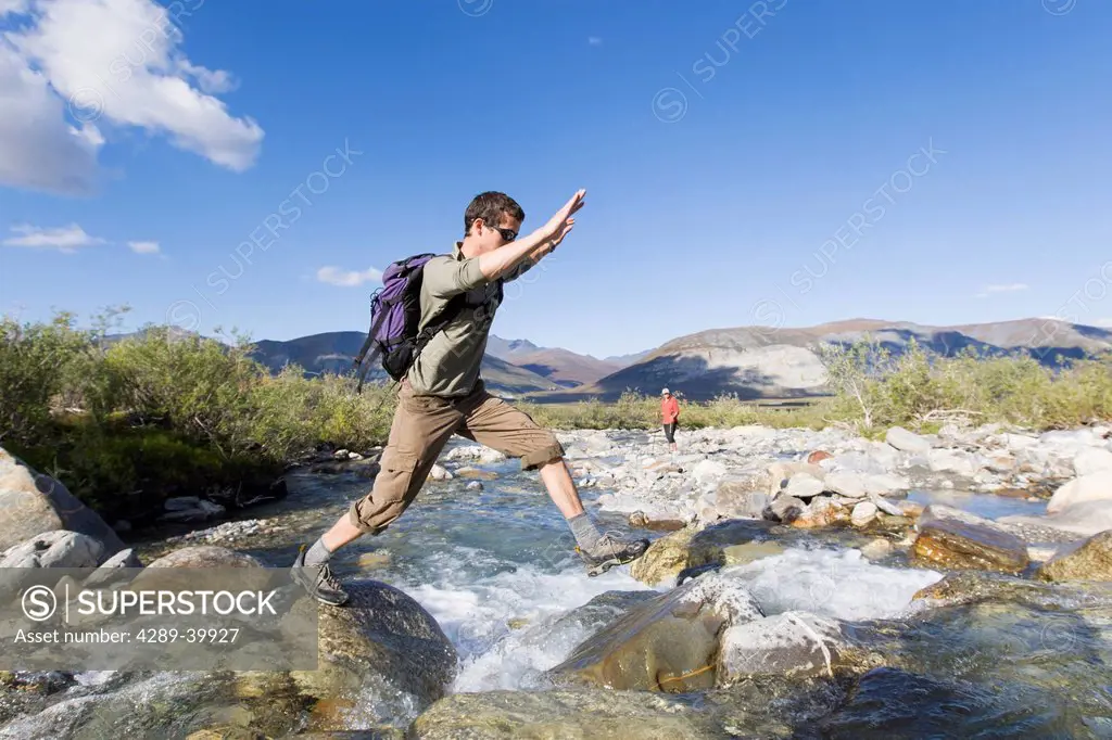 Hiker leaping across rocky creek, Noatak River, Brooks Range, Gates of the Arctic National Park, Northwestern Alaska, above the Arctic Circle, Arctic ...