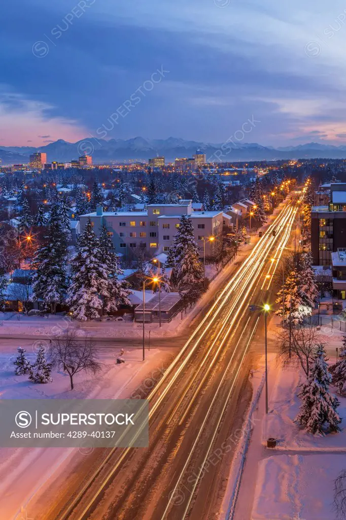 Elevated view of Midtown Anchorage, Looking South from the Parkstrip, traffic streaks in the foreground, Kenai Mountains in the background, twilight, ...