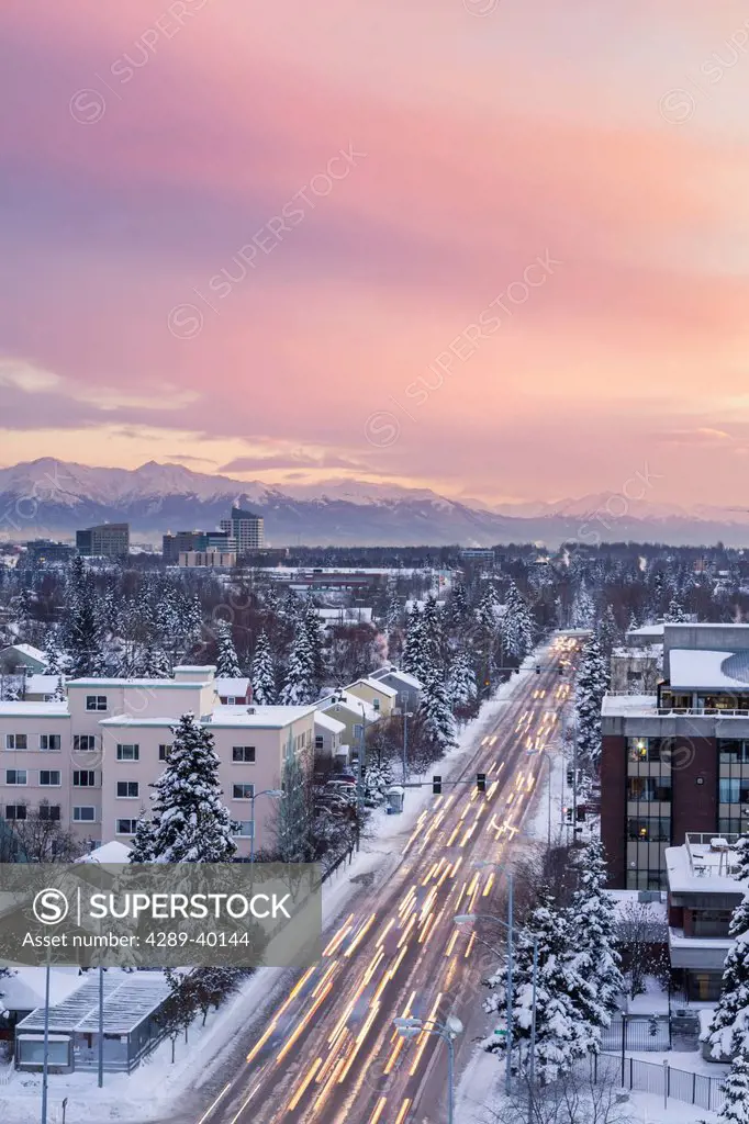 Elevated view of Midtown Anchorage, Looking South from the Parkstrip, traffic streaks in the foreground, Kenai Mountains in the background, sunset, wi...