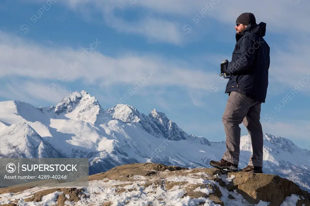 Male hiker taking in the view of the snowcapped Chugach Mountains from the Bodenburg Butte, Matanuska Valley, Southcentral Alaska, Spring