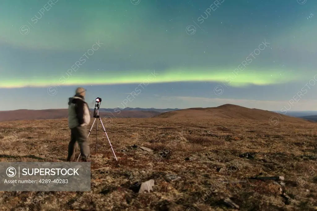 Photographer taking photographs of the Northern Lights above Eagle Summit along the Steese Highway Northeast of Fairbanks, full moon, Pinnell Mountain...