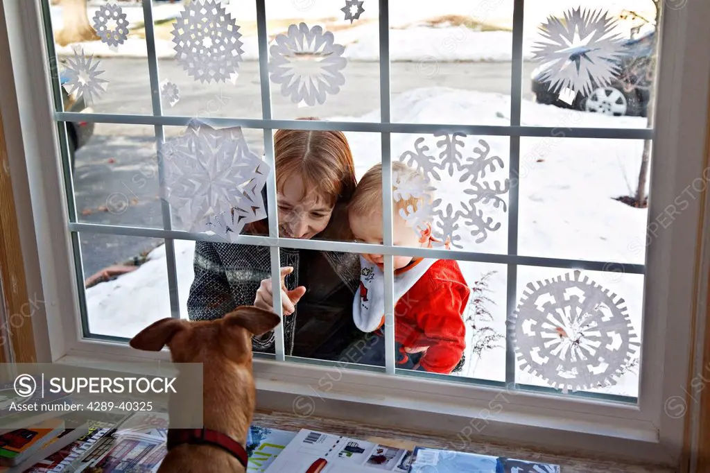 A Woman Hold Her Young Son While Looking Into A Window At A Dog During Wintertime