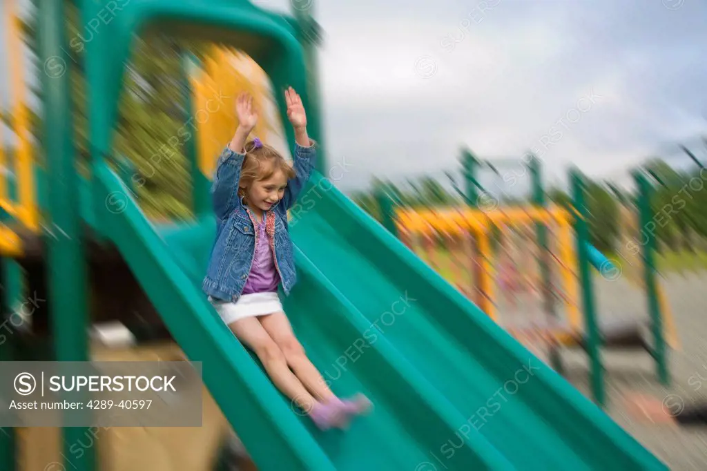 Blurred Motion View Of A Young Girl Playing On A Slide At An Anchorage Playground, Alaska During Summer