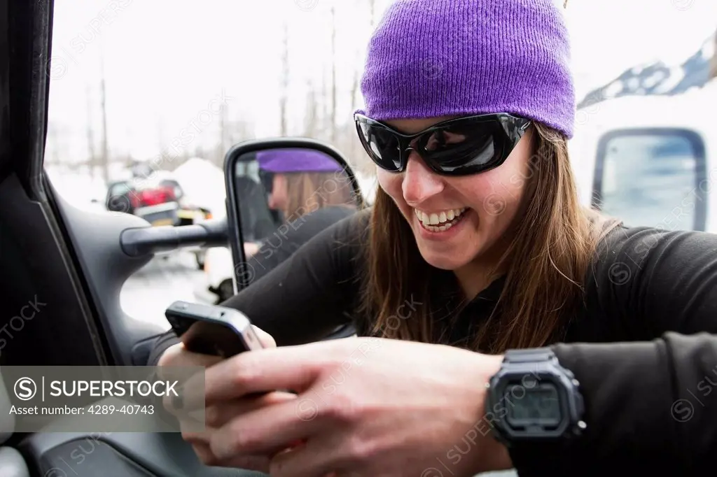 Lauren Georgelos Using Her Smartphone In A Parking Lot While On A Backcountry Snowmobile Ski Trip In The Chugach Mountains In Late Winter, Southcentra...