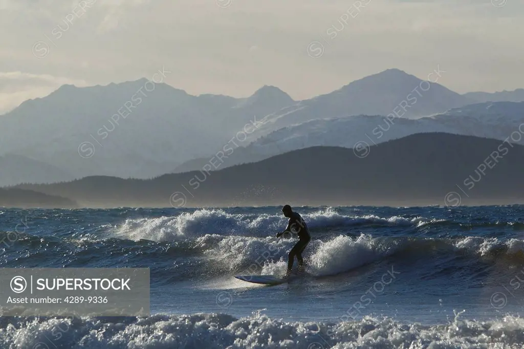 Man surfing along the coastline in Winter with Chilkat Range in the background, Eagle Beach, Southeast Alaska