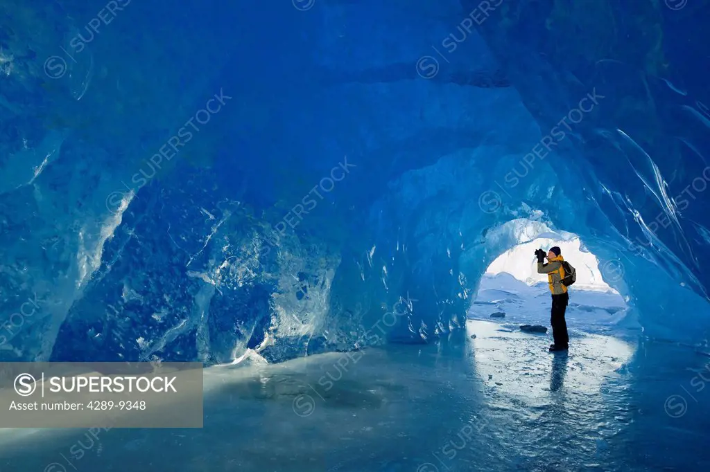 Man photographs inside an ice cave of an iceberg frozen in Mendenhall Lake, Juneau, Southeast Alaska, Winter