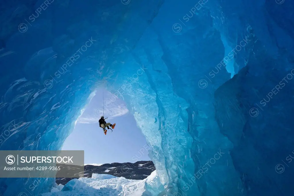 COMPOSITE: View from inside an ice cave of an iceberg frozen in Mendenhall Lake as an ice climber rappels down a rope, Juneau, Southeast Alaska, Winte...