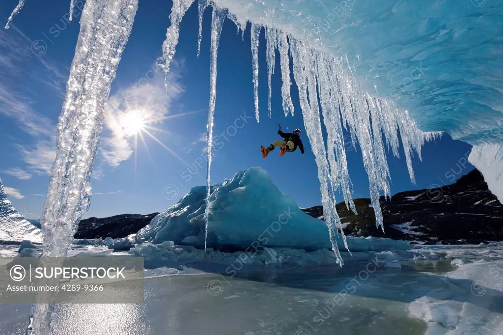 COMPOSITE Sun shines through icicles hanging from the edge of an iceberg as an ice climber rappels over the edge, Mendenhall Lake near the terminus of...