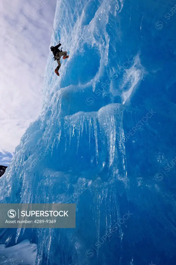 An ice climber ascends the face of a large iceberg frozen into Mendenhall Lake, Juneau, Southeast Alaska, Winter