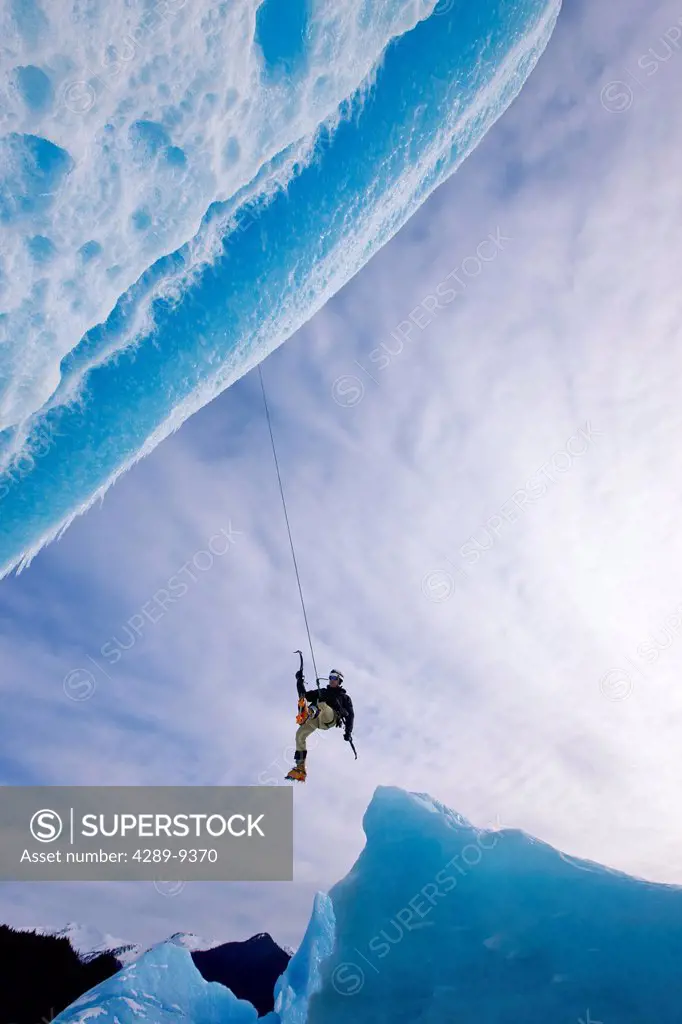 An ice climber swings down from rope to reach face of a large iceberg frozen into Mendenhall Lake, Juneau, Southeast Alaska, Winter