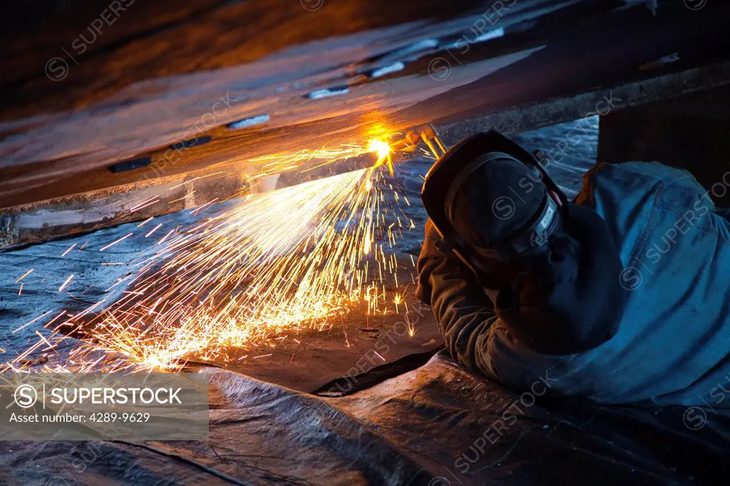 Worker cuts metal fittings off a boat hull using an oxy_acetylene cutting torch, Kodiak Boatyard, Saint Herman Harbor, Kodiak, Near Island, Southwest ...