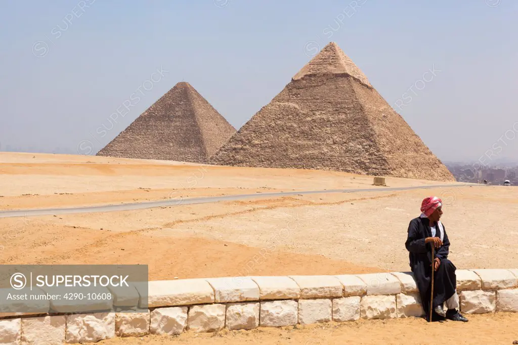 Man sitting on wall in front of the Great Pyramid and Pyramid of Khafre in the Giza Necropolis, Giza, Cairo, Egypt