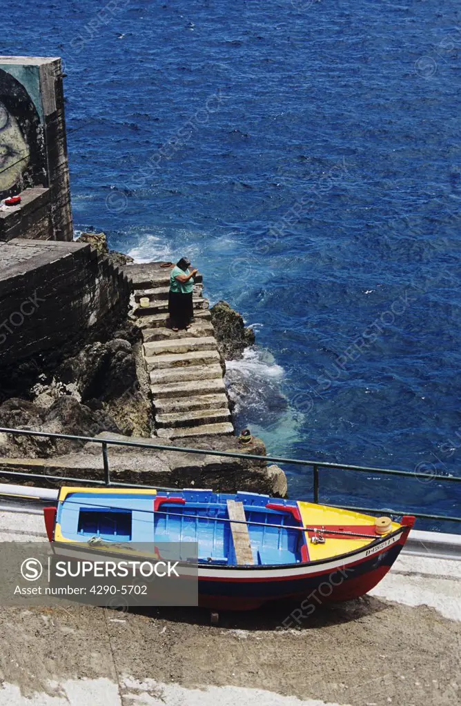 Colourful painted fishing boat on slipway, and lady fishing, Porto Do Moniz, Madeira