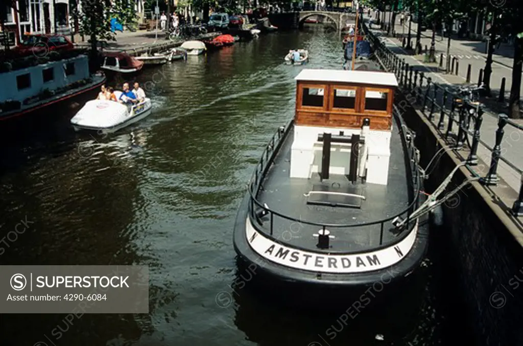 Boat moored on a canal beside a road, tourists in pedalo, Amsterdam, Holland