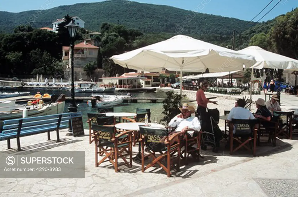 People sitting at outdoor restaurant table beside Kioni harbour, Kioni, Ithaca, Greece