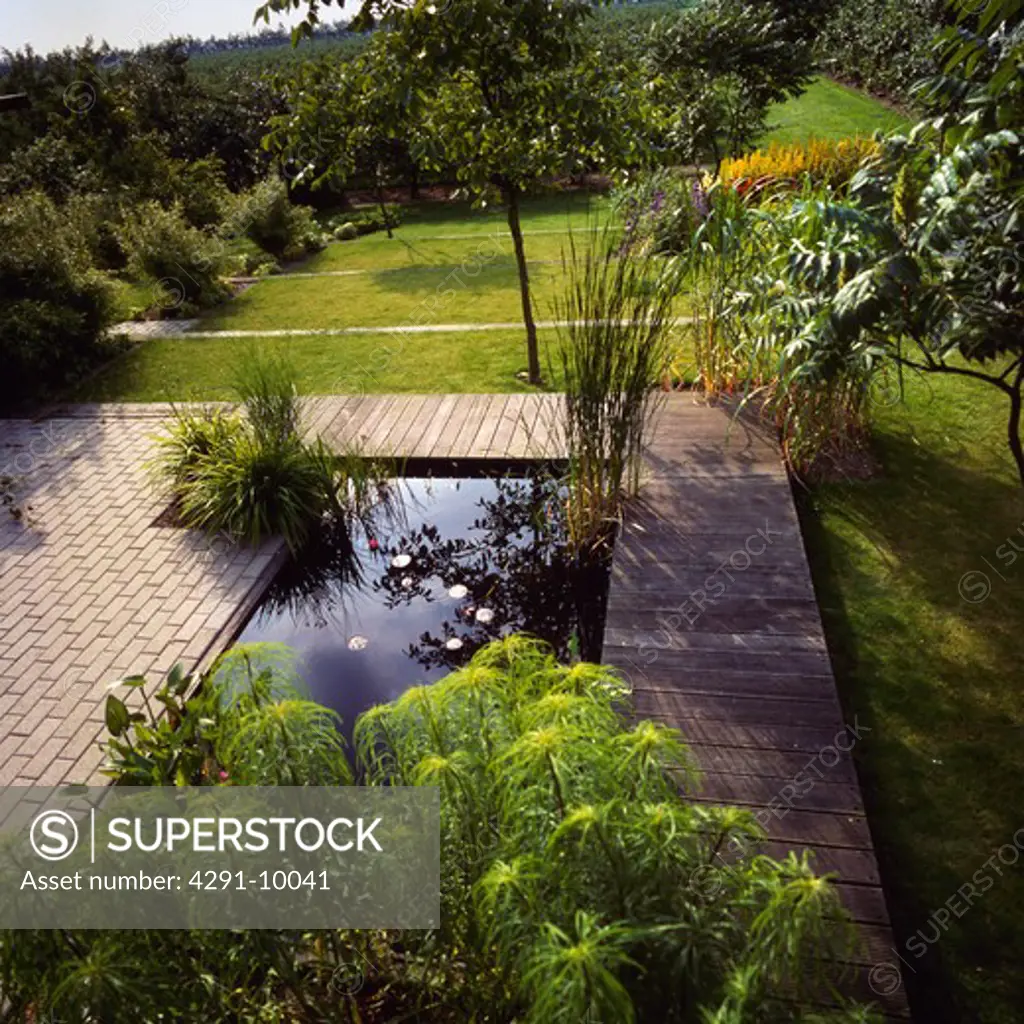 Paving and wooden decking around small rectangular pond in large country garden