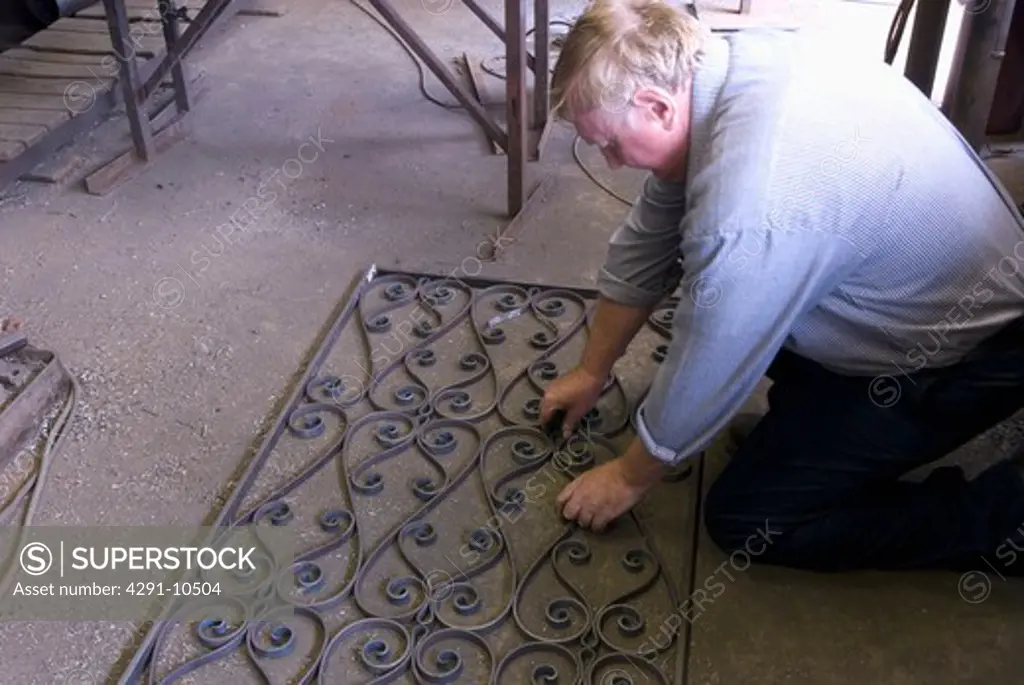 Blacksmith laying out crafted metal scrolls for gate within it's frame on floor of workshop to check for accuracy prior to assembly