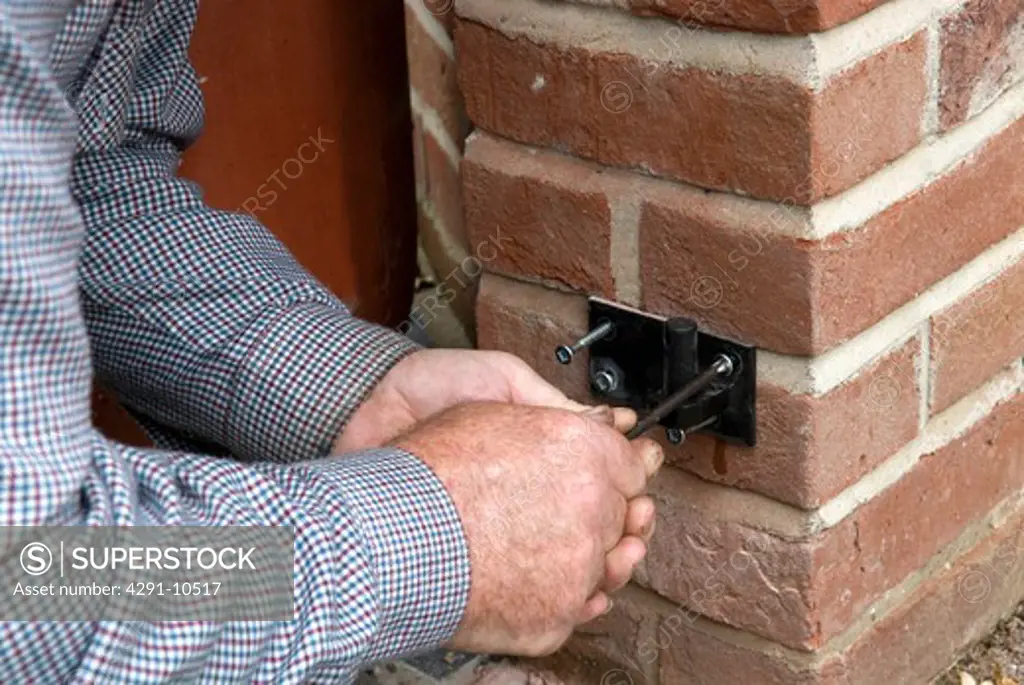 Blacksmith fixing bracket to brickwork using strong screws prior to hanging finished gate on it's hinges