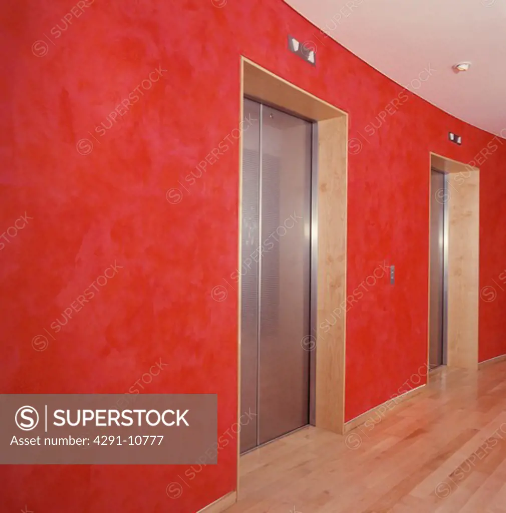 Stainless steel doors on lift in lobby of hotel with red spongeing effect on walls